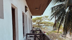 Een houten trap die leidt naar een overdekt balkon met uitzicht op een strand en palmbomen.