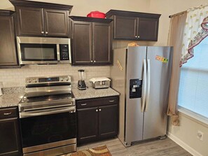 A kitchen with dark cabinets, stainless steel appliances, a microwave, oven, toaster, and a refrigerator.