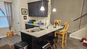 A kitchen with a granite countertop, dark cabinets, a sink, and two bar stools. - Charming Home in La Vergne | Chill and Relax (La Vergne)