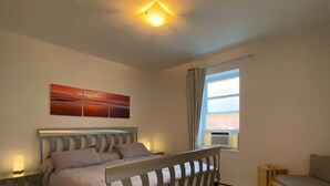 A bedroom with a bed, a bedside table, a chair, a window, and a painting on the wall. - Maison Tamtam (CITQ #: 309507) (Montréal)