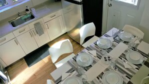 A modern kitchen with white cabinets, a black refrigerator, and a dining area set with plates, glasses, and cutlery. - Maison Tamtam (CITQ #: 309507) (Montréal)