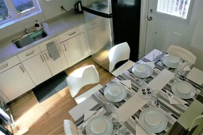 A modern kitchen with white cabinets, a black refrigerator, and a dining area set with plates, glasses, and cutlery. - Maison Tamtam (CITQ #: 309507) (Montréal)