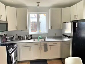 A compact kitchen with white cabinets, a black refrigerator, a microwave, a toaster, and a stove. - Maison Tamtam (CITQ #: 309507) (Montréal)
