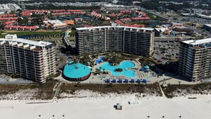 Ett semesterkomplex med flera höga byggnader, ett centralt poolområde och en strand i förgrunden.