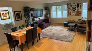 Ein geräumiger Wohnbereich mit Esstisch für vier Personen, einem großen Teppich und einer gemütlichen Sitzecke mit Sofa und Sesseln.