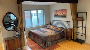 Ein Schlafzimmer mit einem großen Bett, einem Schminktisch, einem Spiegel, einem Fenster mit Vorhängen und einem Gemälde an der Wand.