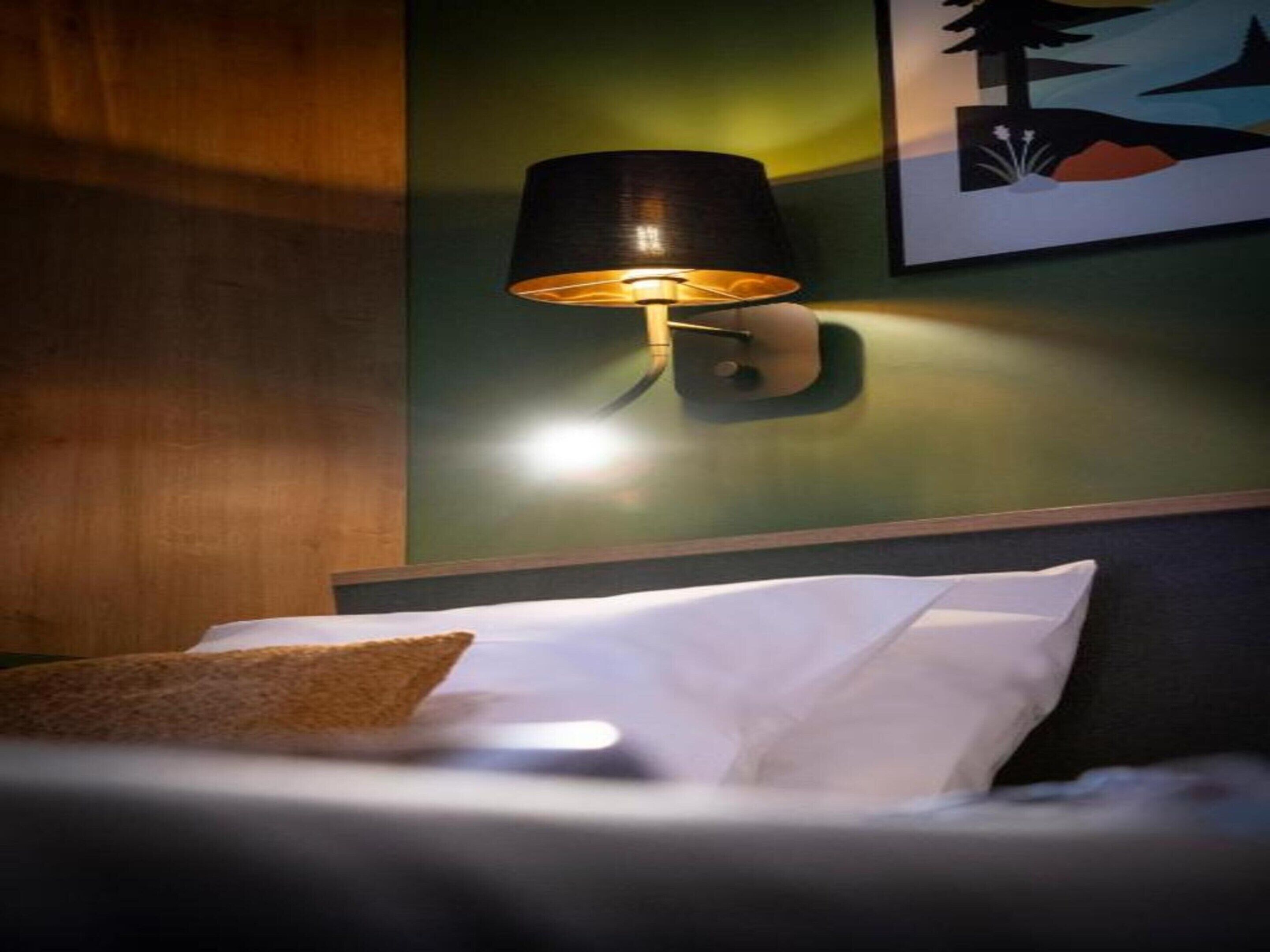 Una habitación de hotel con una cama, una lámpara de pared y un cuadro enmarcado.