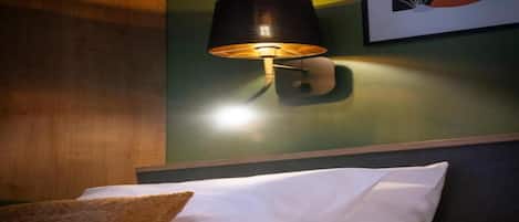 Una habitación de hotel con una cama, una lámpara de pared y un cuadro enmarcado.