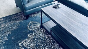 Un soggiorno moderno con un divano blu, un tavolino da caffè e un tappeto decorato.