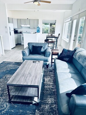 A modern living room with a grey sofa, a coffee table, and a dining area with a table and chairs. - Alaska Vacation Rentals, A downstairs private apartment (Homer)