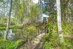 A rustic cabin with a wooden deck, surrounded by a pond and dense forest.