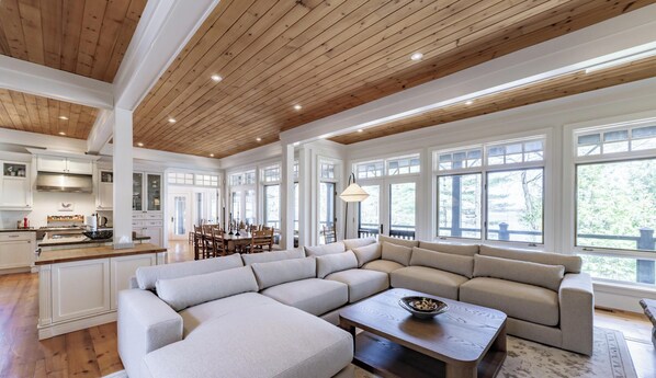 A spacious kitchen with wooden beams, a dining area with a large table, and a seating area with a sofa and coffee table. - Traditional 6 bed 5 bath cottage on Lake Joseph with boathouse & pickleball! (MacTier)