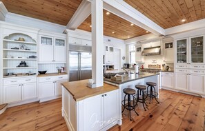 Un'ampia cucina con mobili bianchi, soffitto in legno e isola centrale con sgabelli.