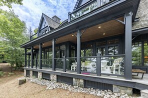 A modern house with a covered porch, stone foundation, and large windows. - Traditional 6 bed 5 bath cottage on Lake Joseph with boathouse & pickleball! (MacTier)