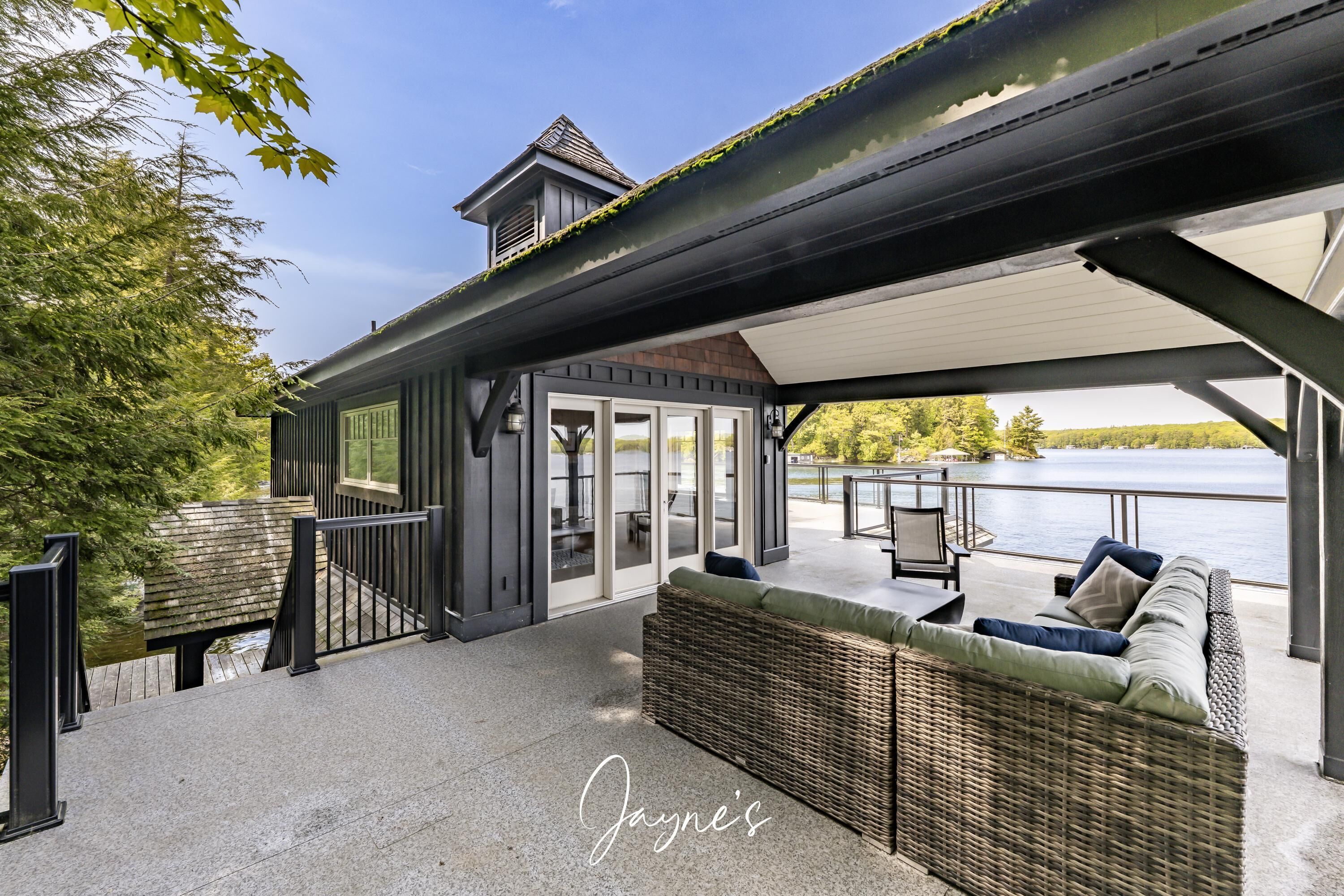 A covered outdoor seating area with a wicker sofa and a table, overlooking a body of water.