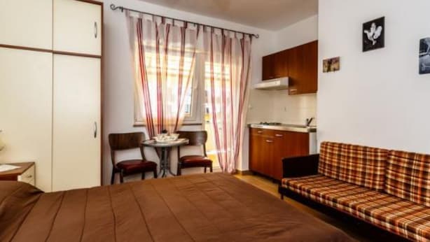 A bedroom with a bed, a sofa, a small table, and a kitchenette.