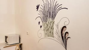 A wall with a decorative floral decal, a microwave, a lamp, and a red cushion on a wooden bench.
