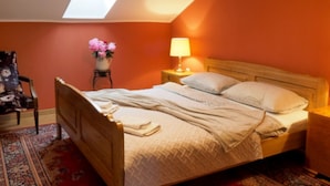 Et soveværelse med ovenlys, en seng med puder, et natbord med lampe, en stol og en vase med blomster.