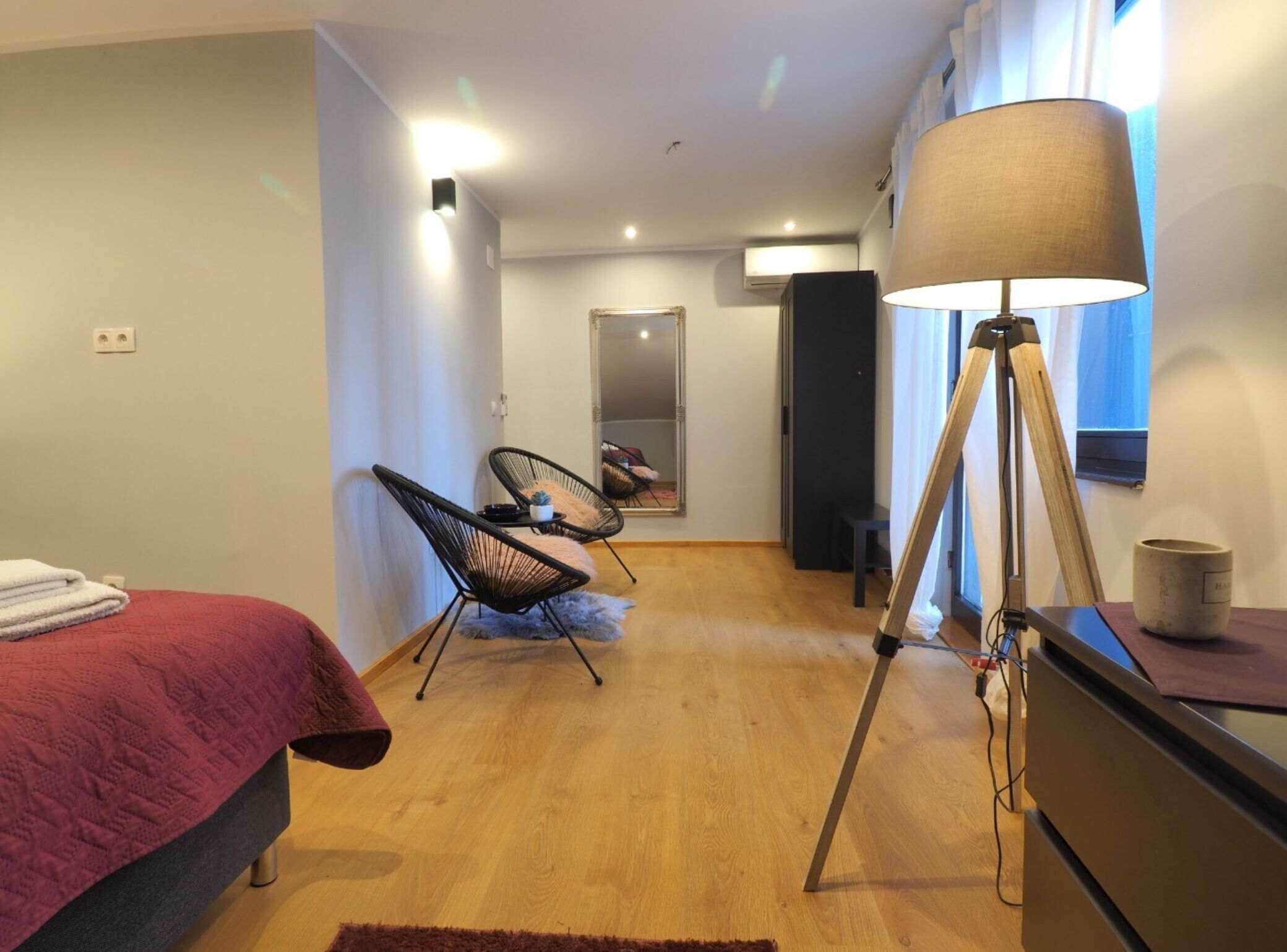 Een moderne slaapkamer met een bed, twee stoelen, een lamp en een spiegel.