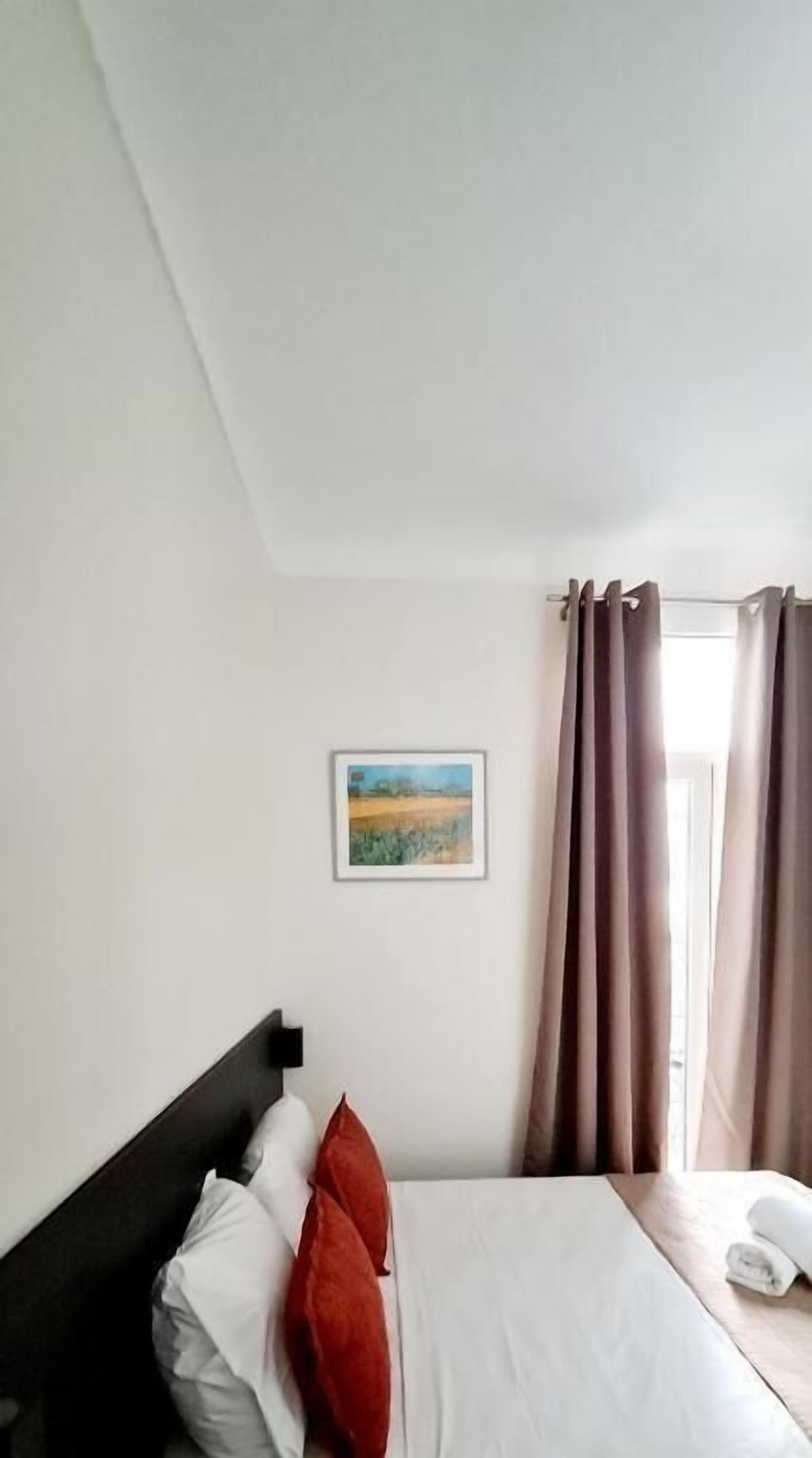 A hotel room with a bed, a painting on the wall, and a window with curtains.