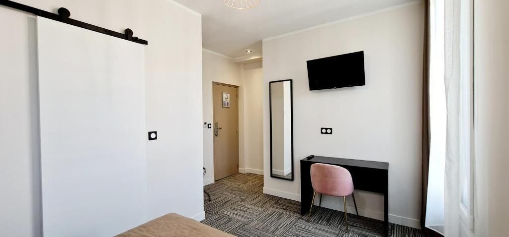 Hotelkamer met een schuifdeur, een bureau met stoel, een flatscreen televisie aan de muur en een grote spiegel.