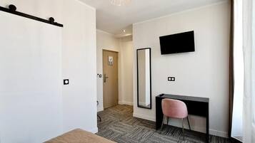 Hotelkamer met een schuifdeur, een bureau met stoel, een flatscreen televisie aan de muur en een grote spiegel.