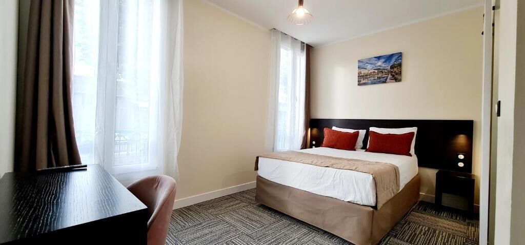 A hotel room with a bed, a desk, and a window with curtains.