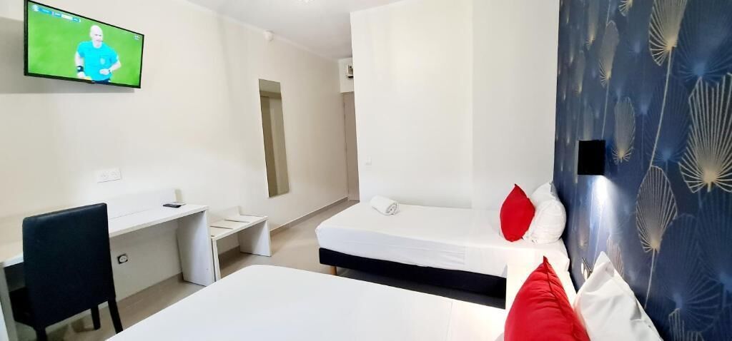 Een hotelkamer met twee bedden, een bureau, een stoel en een televisie aan de muur.