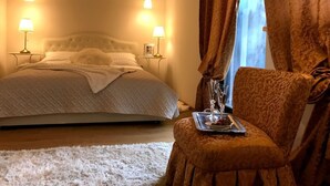 Ein Schlafzimmer mit einem Bett, zwei Nachttischlampen, einem Stuhl mit einem Tablett Essen und einem Fenster mit Vorhängen.