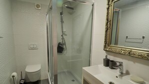 Ein Badezimmer mit Duschkabine, Toilette, Waschbecken mit Spiegel und Handtuchhalter.