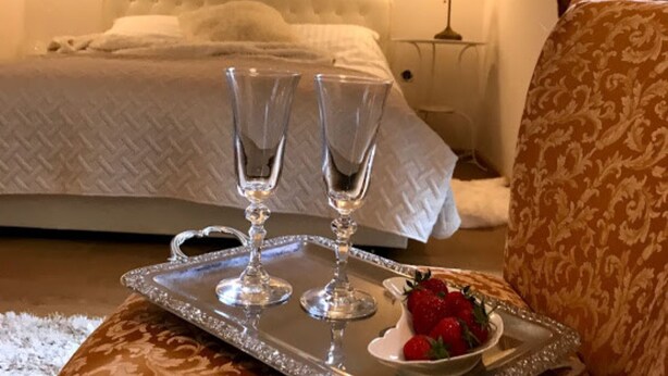 Ein Hotelzimmer mit einem Bett, einem Nachttisch mit Lampe und einem Tablett mit zwei Gläsern sowie einer Schale Erdbeeren.
