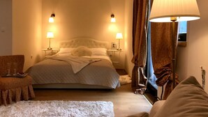 Ein ordentlich eingerichtetes Schlafzimmer mit einem großen Bett, zwei Nachttischlampen, einem Sessel und einem Fenster mit Vorhängen.