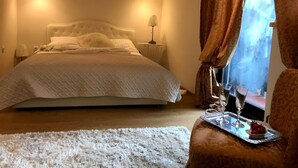 Ein Schlafzimmer mit einem großen Bett, zwei Nachttischlampen, einem Nachttisch, einem Fenster mit Vorhängen und einer Schale mit Gläsern und Erdbeeren auf einem Stuhl.