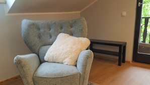 A light grey upholstered armchair with a fluffy white pillow, positioned in a room with a wooden floor and a patterned rug. - Apartments & Rooms Latin - Quadruple Room (Plaski)