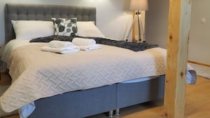 A neatly made bed with a grey headboard, two wall-mounted lamps, and a floor lamp. - Apartments & Rooms Latin - Quadruple Room (Plaski)