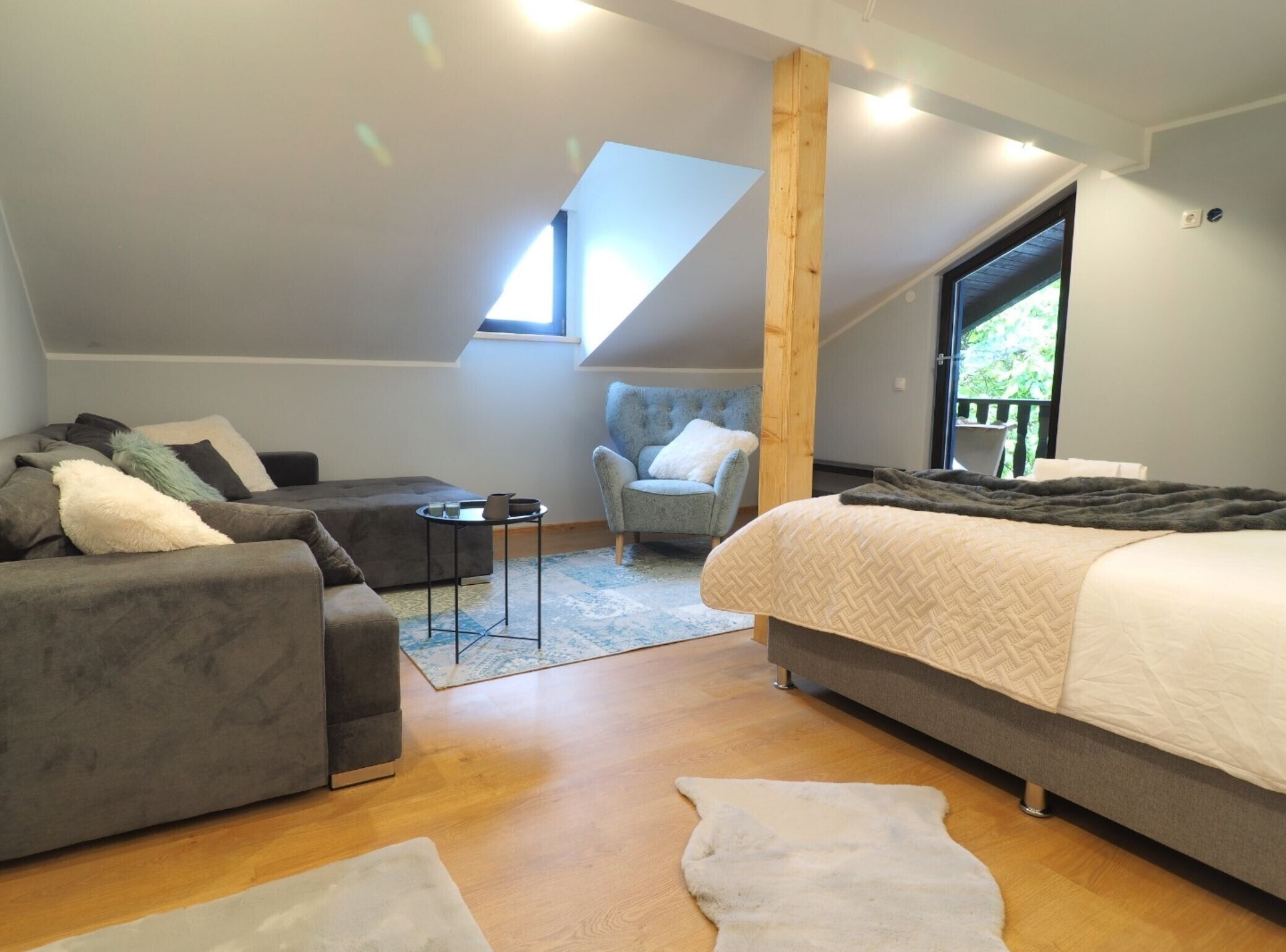 Ett modernt sovrum i loftstil med en stor säng, en grå soffa, ett litet bord och en stol.