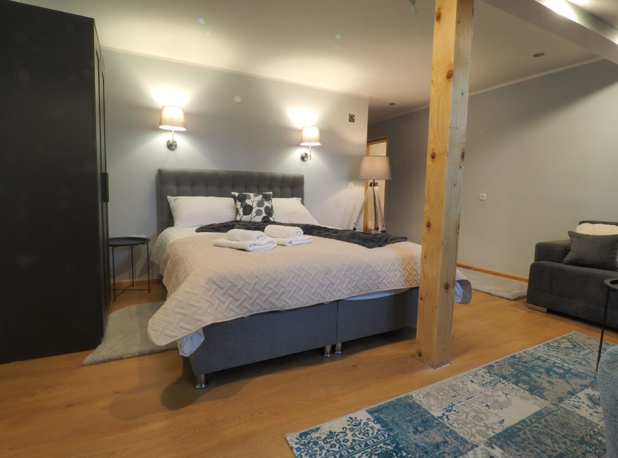 Quarto com cama, luminárias de cabeceira, uma cadeira e um sofá.
