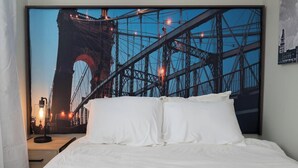Un dormitorio con una cama grande, ropa de cama blanca y un cabecero con un mural de un paisaje urbano.