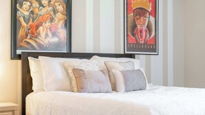 Ein ordentlich bezogenes Bett mit vielen Kissen und einem gerahmten Disney-Filmposter darüber.