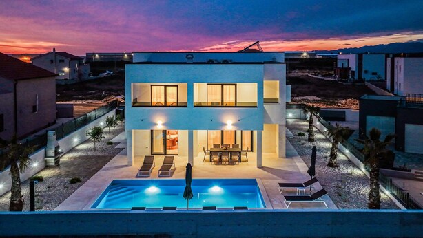 Ein modernes, zweistöckiges Haus mit Swimmingpool, Außenbereich und Blick auf den Sonnenuntergang.