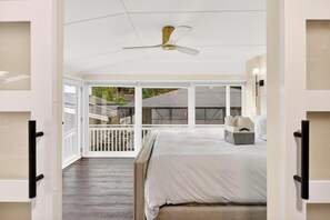 A bedroom with a bed, a ceiling fan, a window with a view of a balcony, and a nightstand with a lamp. - Luxury Home on Dora Lake – 2 Min to Downtown Mount Dora (Mount Dora)