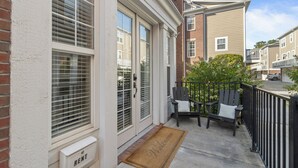 A residential building with a front door, a welcome mat, and a small outdoor seating area with two chairs and a bench.