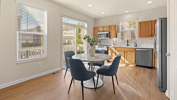 A modern kitchen with wooden cabinets, a stainless steel refrigerator, and a dining area with a round table and chairs.