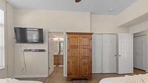 A bedroom with two beds, a wooden wardrobe, a television mounted on the wall, and white doors.
