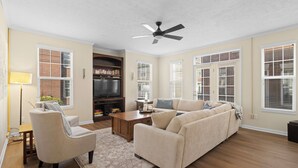 A living room with a sectional sofa, a coffee table, a TV, and a ceiling fan.