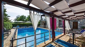 Ein Poolbereich mit Steinmauer, Liegestühlen und einer überdachten Sitzecke.
