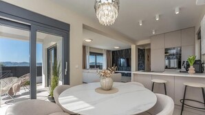 Uma cozinha moderna com bancada de mármore, sala de jantar com mesa redonda e cadeiras estofadas, e varanda com vista para as montanhas.