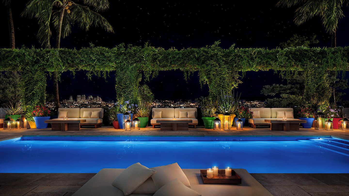 Un área junto a la piscina con sillones de descanso y plantas en macetas.