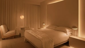 A modern hotel room with a large bed, a small round table, a chair, and a nightstand with a lamp. - PUBLIC West Hollywood (West Hollywood)