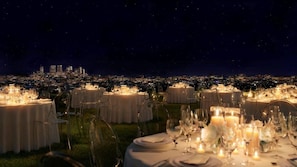 An outdoor dining area with round tables set for a meal, featuring candles and clear glassware. - PUBLIC West Hollywood (West Hollywood)